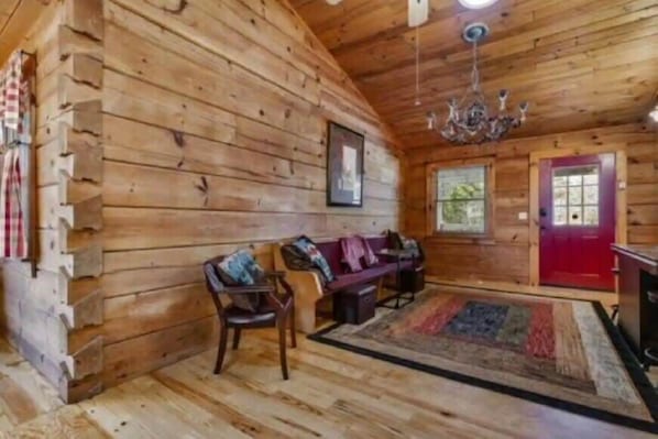 A log cabin interior with a wooden floor, a red door, a chandelier, a bench, and a rug.