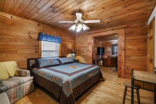 Een slaapkamer in een houten chalet met een bed, een klein tafeltje en een plafondventilator.