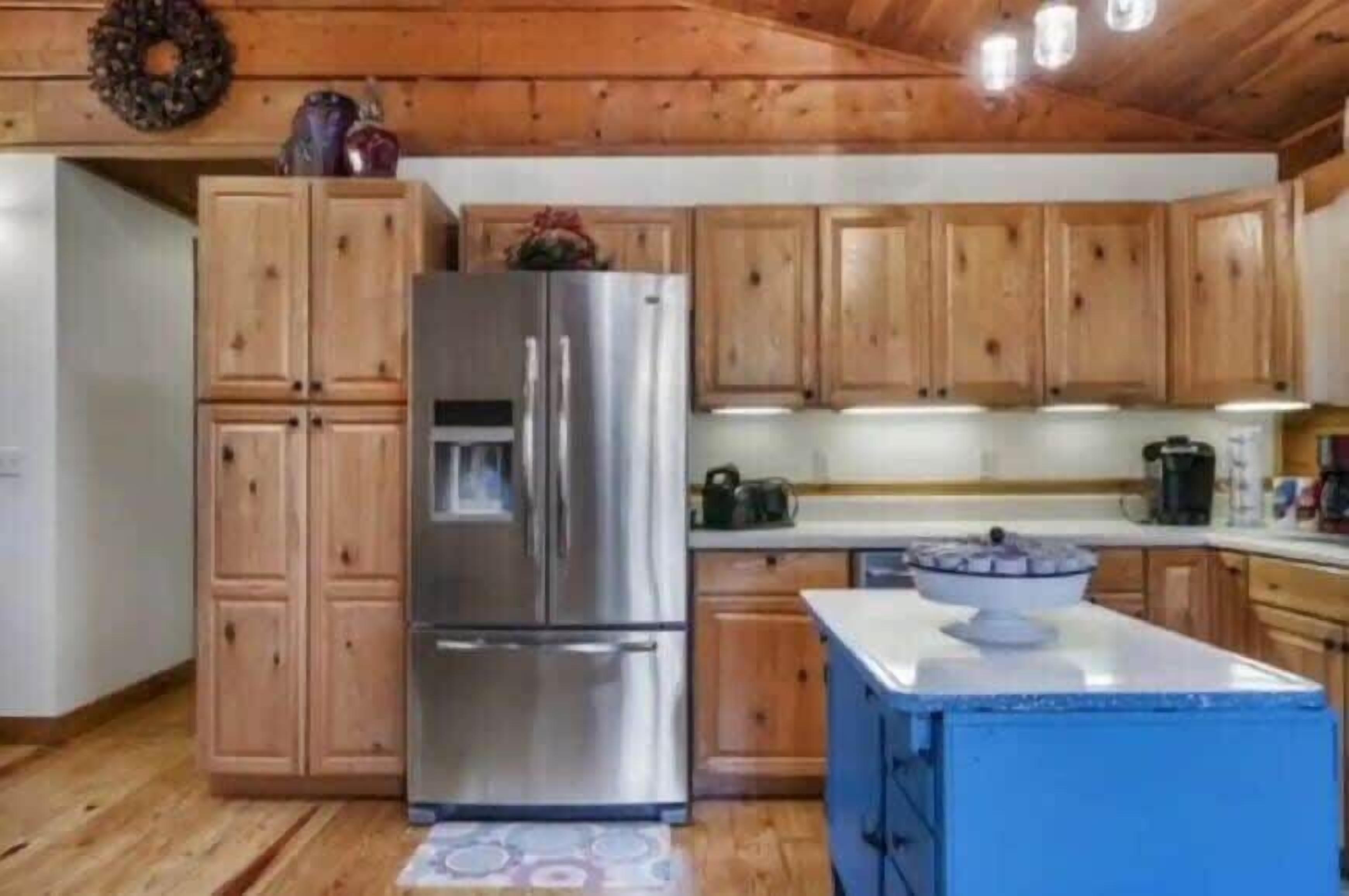 Een keuken met houten kastjes, een roestvrijstalen koelkast en een blauw kookeiland.
