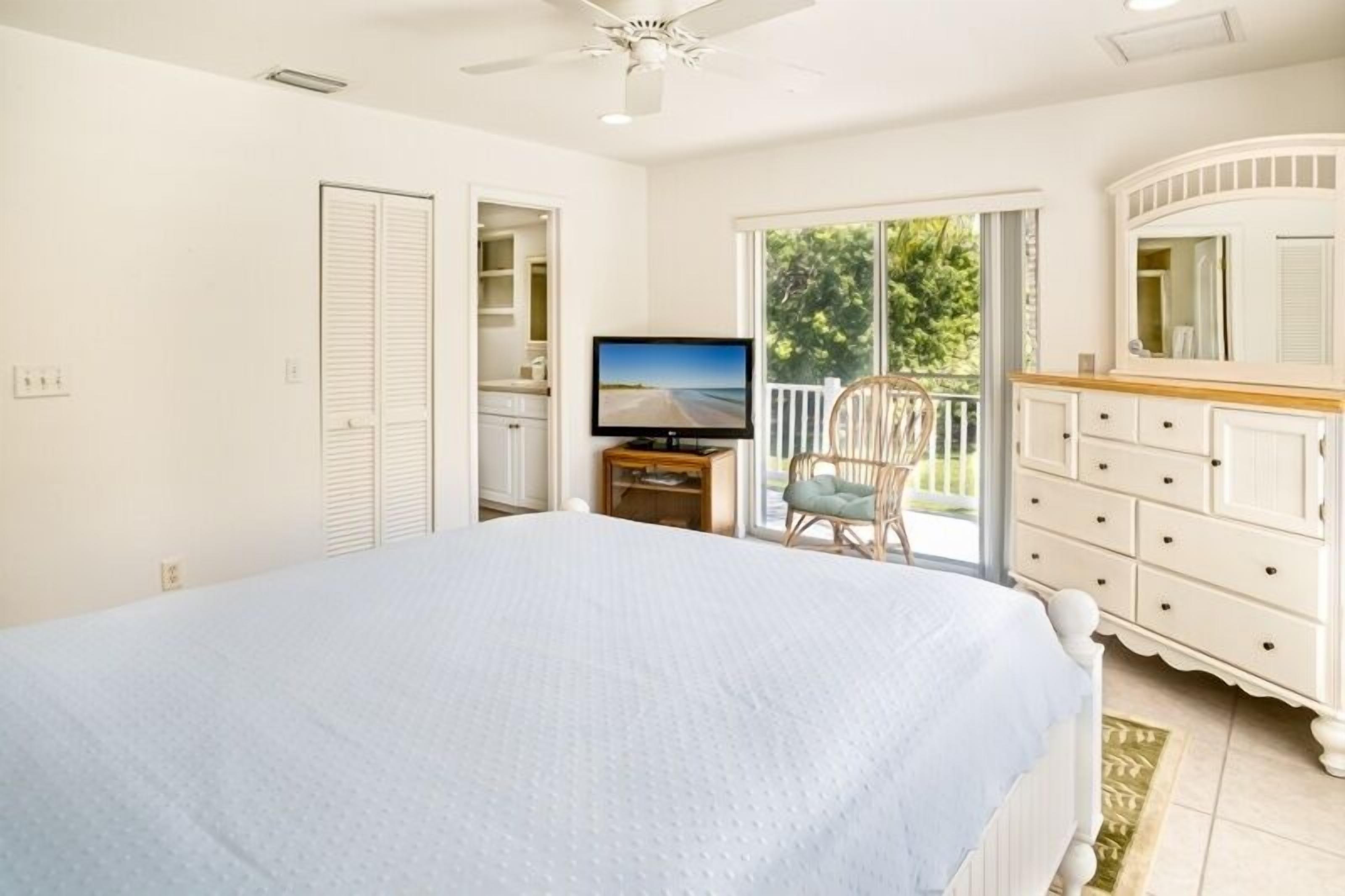Un dormitorio con cama, televisor, cómoda y balcón con vistas al exterior.
