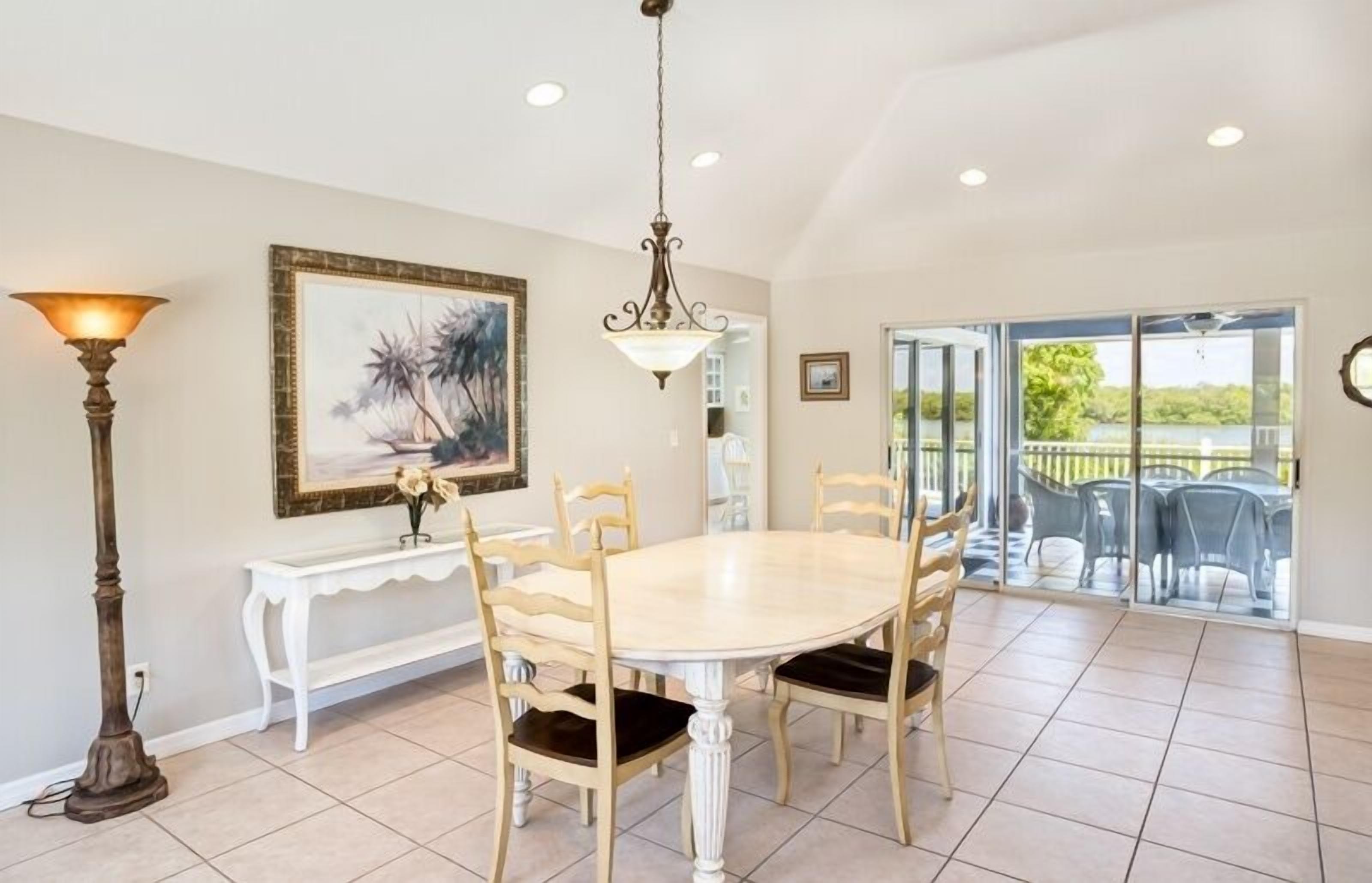 Un coin repas comprenant une table ronde, six chaises, une console blanche, un lampadaire et un tableau accroché au mur.