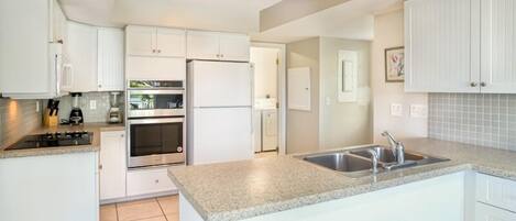 A modern kitchen with white cabinets, a granite countertop, stainless steel appliances, and a built-in sink.