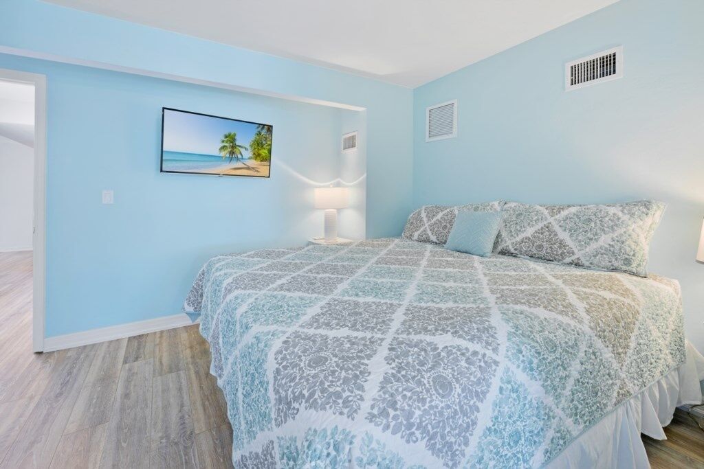 A bedroom with a bed, a nightstand, a lamp, and a picture of a beach scene on the wall.