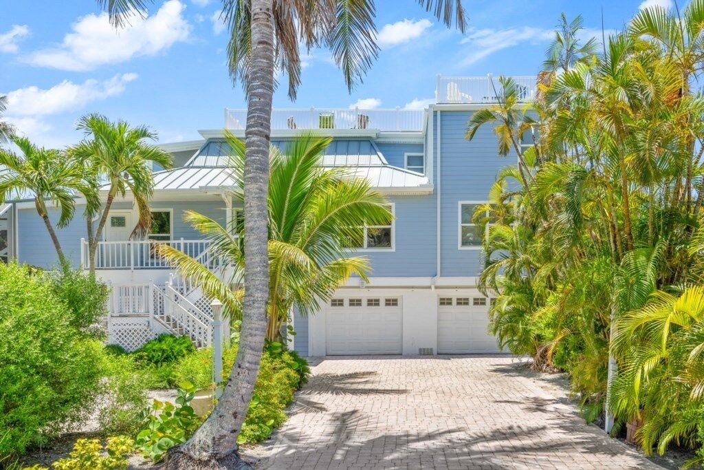 A two-story house with a paved driveway, surrounded by palm trees and greenery.