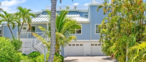 A two-story house with a paved driveway, surrounded by palm trees and greenery.