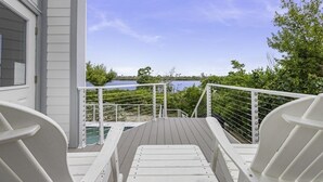 Eine Holzterrasse mit weißen Geländern führt zu einem Gewässer, umgeben von viel Grün.