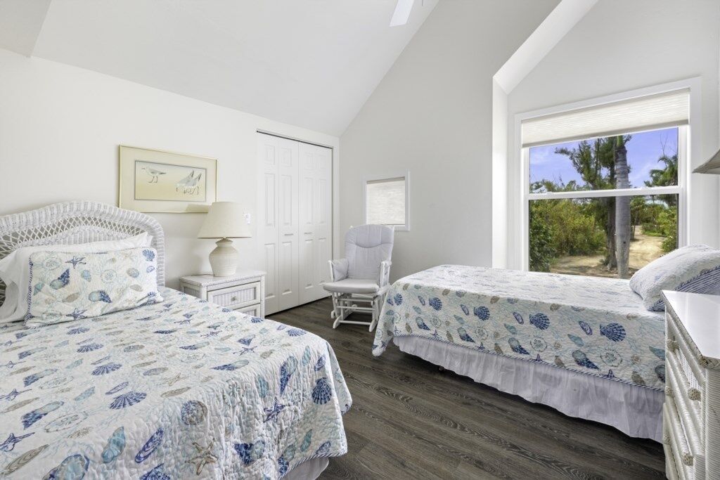 Une chambre avec deux lits, une chaise, une table de chevet, une lampe et une fenêtre donnant sur un paysage verdoyant.