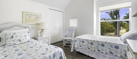 Une chambre avec deux lits, une chaise, une table de chevet, une lampe et une fenêtre donnant sur un paysage verdoyant.