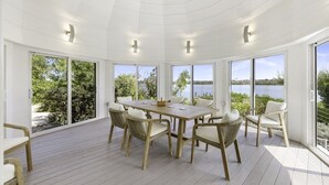 Ein geräumiges Zimmer mit einem großen Holztisch und Korbstühlen, große Fenster mit Seeblick und einer weißen Decke mit Einbautenbeleuchtung.