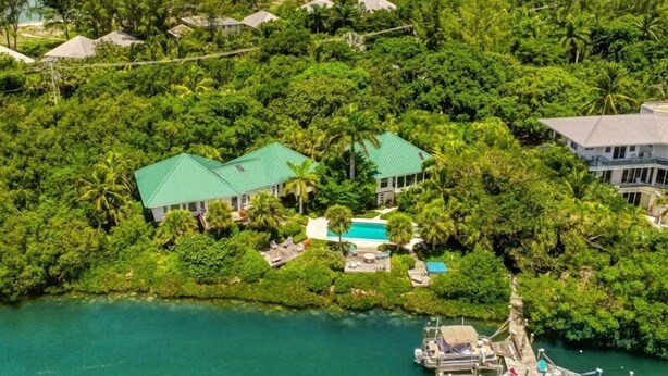 An aerial view of a tropical resort with multiple buildings surrounded by dense greenery, a clear blue pool, and a dock with boats. - Little Current 3 Bedroom Home by RedAwning (Captiva)