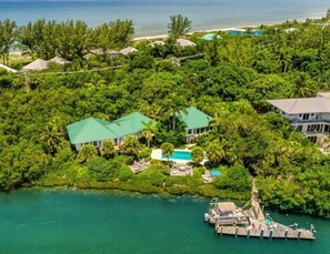An aerial view of a tropical resort with multiple buildings surrounded by dense greenery, a clear blue pool, and a dock with boats. - Little Current 3 Bedroom Home by RedAwning (Captiva)