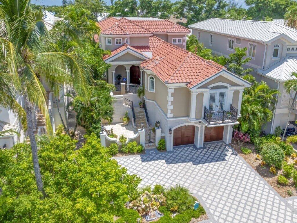 A large, two-story house with a red-tiled roof, a covered front porch, and a landscaped front yard with palm trees and shrubs.