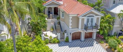 A large, two-story house with a red-tiled roof, a covered front porch, and a landscaped front yard with palm trees and shrubs.