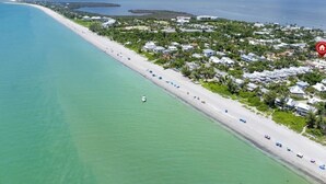 Luftaufnahme einer Küstenregion mit einem langen Sandstrand, einem Jachthafen und Wohngebäuden.