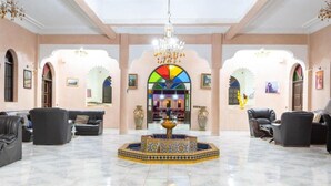 A spacious lobby with a central fountain, comfortable seating, and a view into a dining area. - Hotel Riad Qodwa (Sidi Abdallah Ghiat)