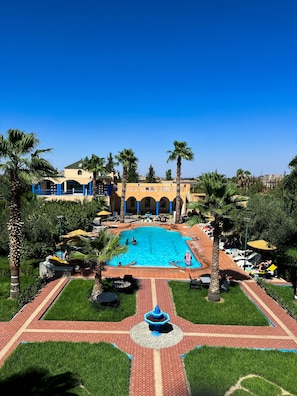 A swimming pool surrounded by palm trees and a building with arches. - Hotel Riad Qodwa (Sidi Abdallah Ghiat)
