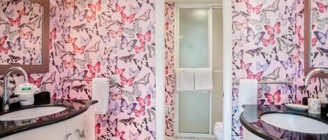 Un baño con papel tapiz estampado con motivos de mariposas, dos lavamanos y una puerta de ducha de vidrio.