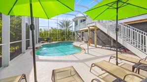 An indoor swimming pool with a glass ceiling, surrounded by lounge chairs and bright green umbrellas. - Osprey House 4 Bedroom Home by RedAwning (Sanibel)