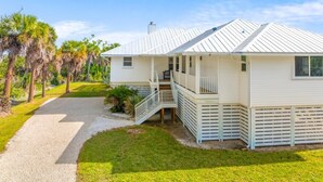 A row of white cabins with a metal roof, a gravel path, and palm trees in the background. - Osprey House 4 Bedroom Home by RedAwning (Sanibel)