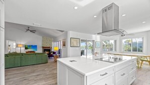 A modern kitchen with white cabinetry, a central island, and a large window. - Osprey House 4 Bedroom Home by RedAwning (Sanibel)