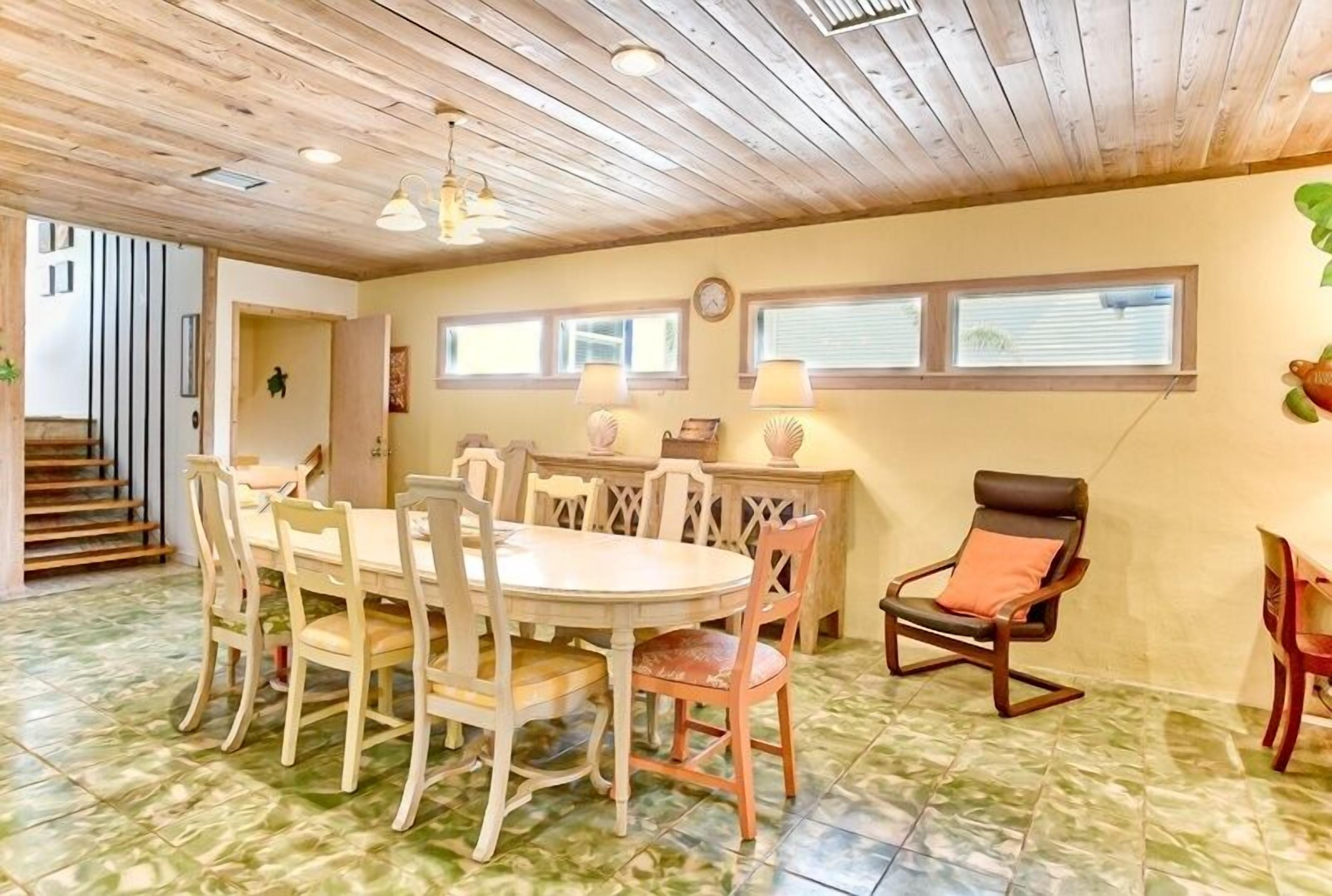 A dining area with a wooden ceiling, a round table with chairs, and a chair with a cushion.