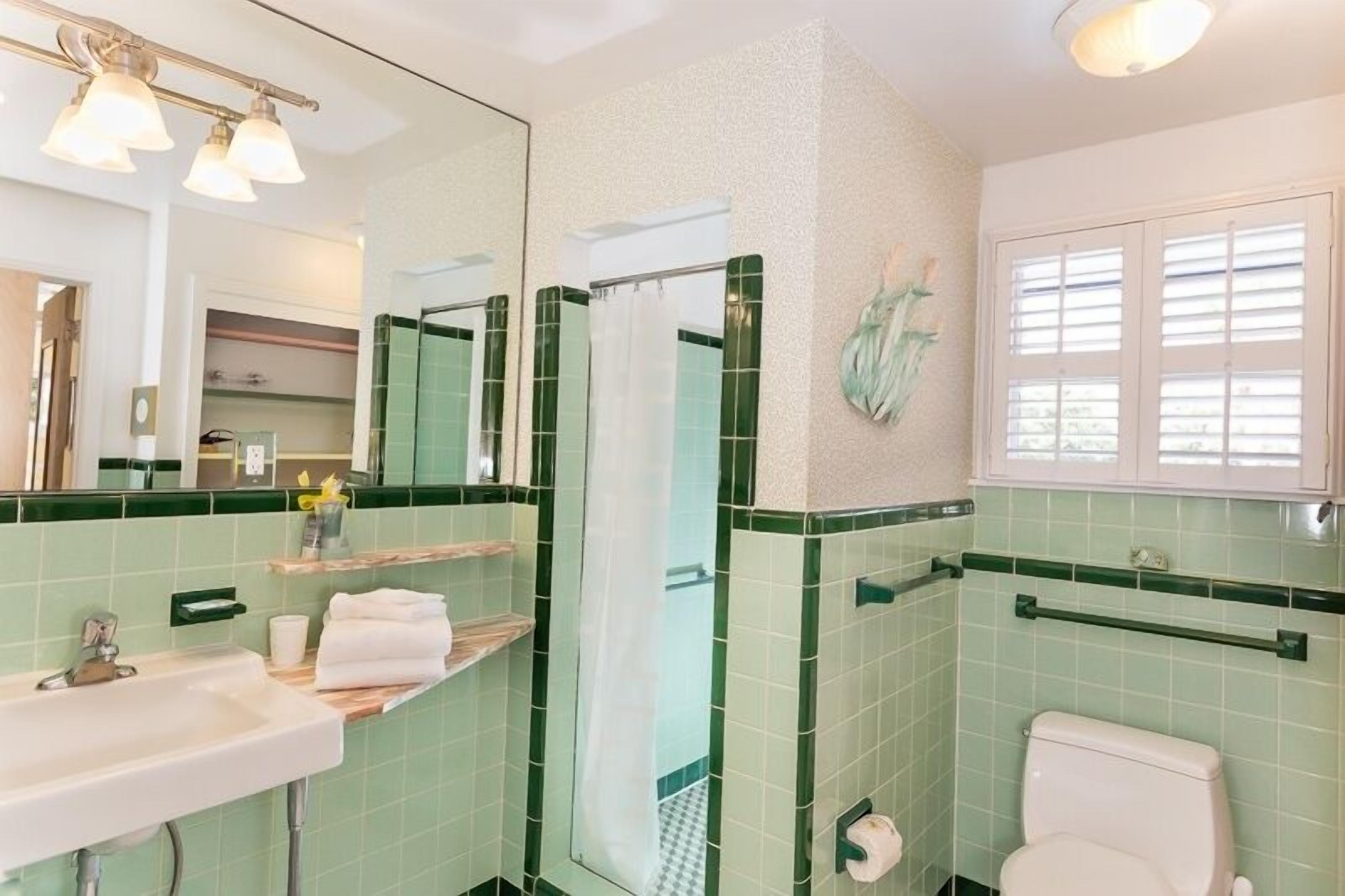 A bathroom with a sink, mirror, shower, toilet, and a window.