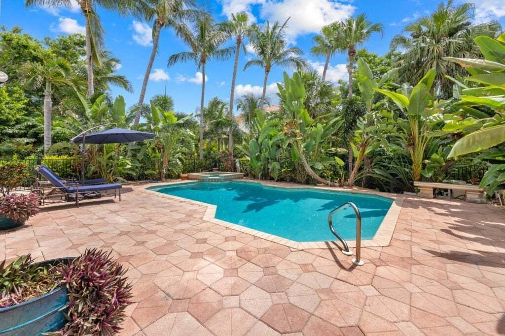 Una piscina con un borde de baldosas, rodeada de palmeras y plantas tropicales.