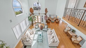 Een ruime woonkamer met uitzicht op de oceaan, een balkon met rieten meubels en een moderne kroonluchter.