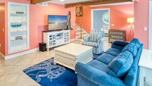A living room with a blue couch, a TV, a bookshelf, and a staircase. - Lollipop 3 Bedroom Home by RedAwning (Captiva)