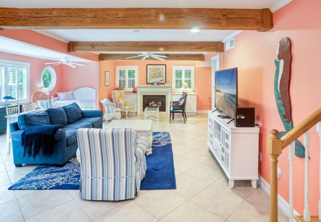 Una sala de estar con sofá, sillón, reposapiés, chimenea, televisor y una escalera.