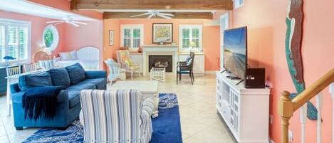 Una sala de estar con sofá, sillón, reposapiés, chimenea, televisor y una escalera.