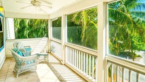 A covered outdoor area with a ceiling fan, a wicker chair with cushions, and a view of palm trees. - Lollipop 3 Bedroom Home by RedAwning (Captiva)