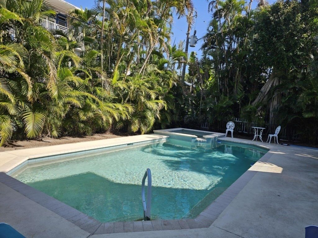 Una piscina rectangular con agua azul cristalina, rodeada de exuberante vegetación y palmeras.