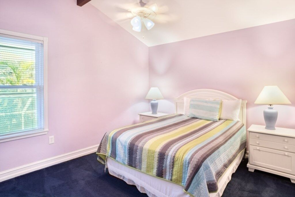 A bedroom with a bed, two bedside tables, a window, and a ceiling fan.