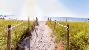 A sandy beach path with footprints leading to the ocean, surrounded by greenery and a clear sky. - Lollipop 3 Bedroom Home by RedAwning (Captiva)
