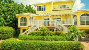 A two-story yellow house with a white porch and a staircase leading to the upper level. - Ark 3 Bedroom Condo by RedAwning (Captiva)