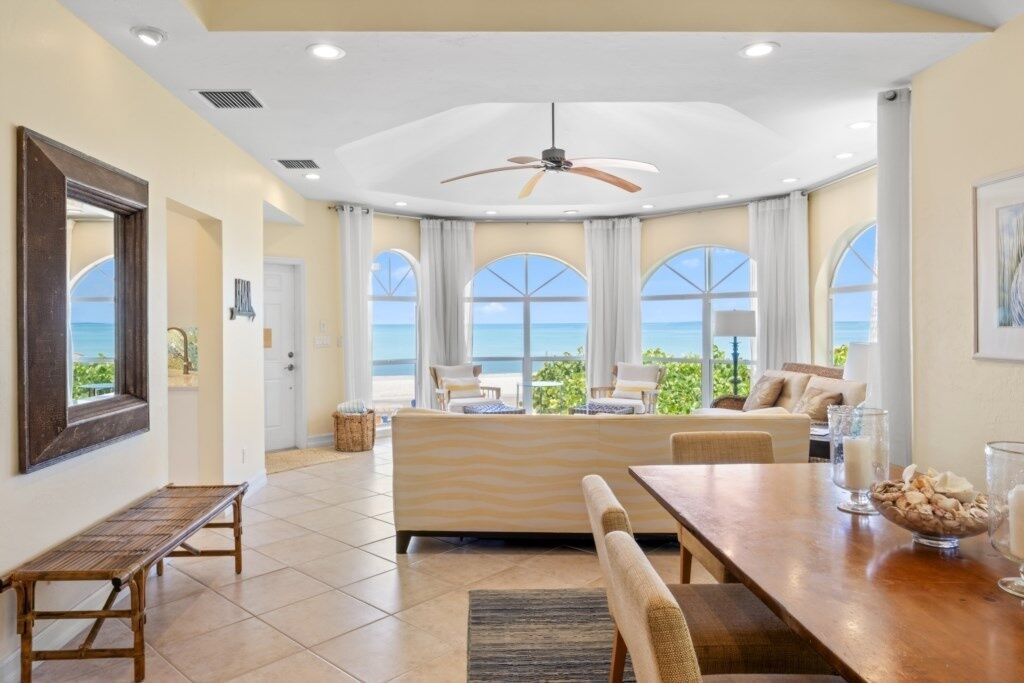A spacious living area with a large window overlooking the sea, a ceiling fan, and a dining table with chairs.