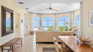 A spacious living area with a large window overlooking the sea, a ceiling fan, and a dining table with chairs. - Ark 3 Bedroom Condo by RedAwning (Captiva)