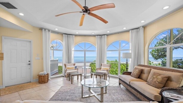 A spacious living room with a large window offering a view of the ocean, a ceiling fan, and a cozy seating area with a sofa and chairs. - Ark 3 Bedroom Condo by RedAwning (Captiva)