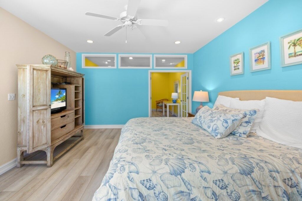 A bedroom with a bed, a ceiling fan, a wooden cabinet, and a television.