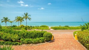 A paved pathway leading to a beach with palm trees and lush greenery. - Ark 3 Bedroom Condo by RedAwning (Captiva)