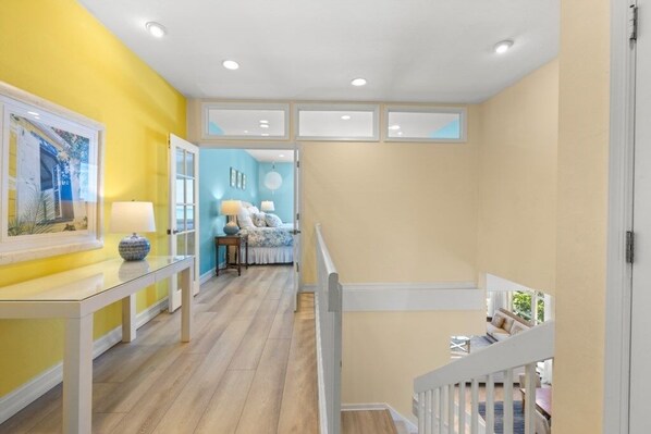 A bright hallway with a yellow wall, a white bench, and a staircase leading to a lower level.