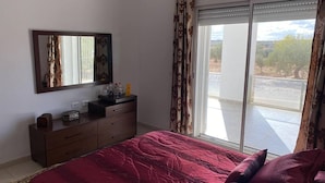 A bedroom with a large bed, a dresser, a mirror, and a sliding glass door leading to an outdoor area. - Cheerful 2-bedroom Villa With Pool (Nasrallah)