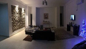 A living room with a stone wall, a sofa, a television, and a small Christmas tree. - Cheerful 2-bedroom Villa With Pool (Nasrallah)