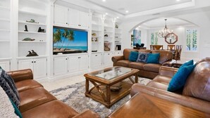 A spacious living room with leather sofas, a glass coffee table, and white cabinetry with shelves.