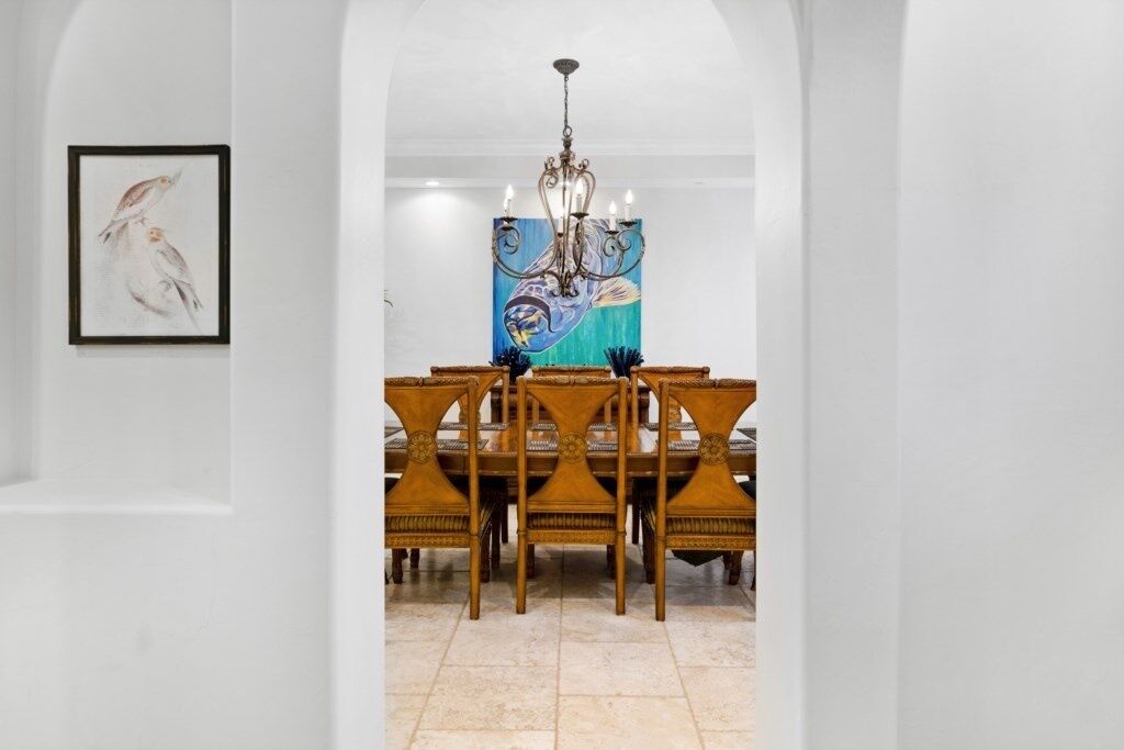 A dining area with a wooden table and chairs, a chandelier, and a painting on the wall.
