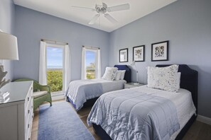 A bedroom with two beds, a desk, a chair, and a ceiling fan.