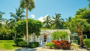 A single-story house with a front porch, surrounded by palm trees and tropical vegetation.