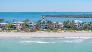 A beachfront property with multiple houses, a clear view of the ocean, and a bird flying overhead. - Captiva Grace 5 Bedroom Home by RedAwning (Captiva)