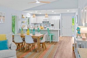 A modern kitchen with white cabinets, a dining table with chairs, and a colorful striped rug.